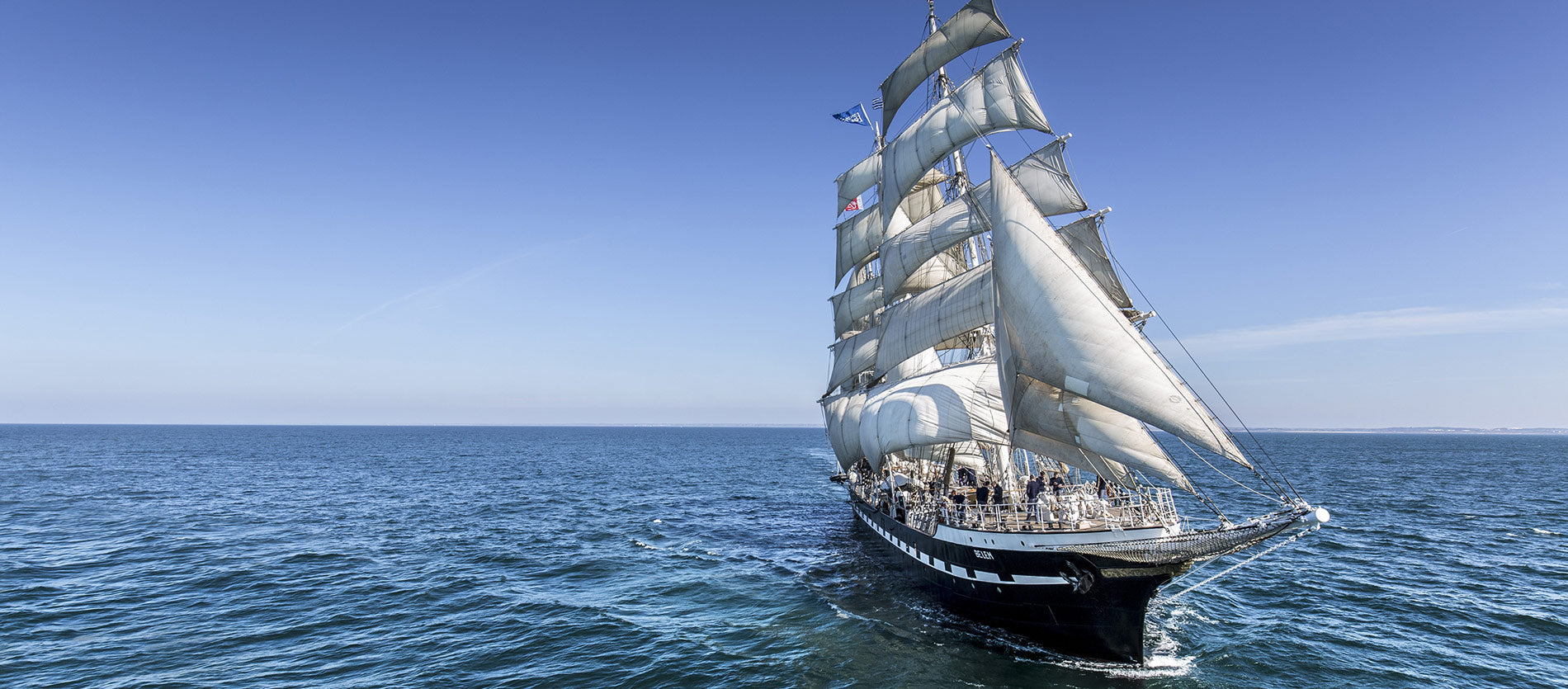A tall ship under full sail on a calm sea with clear blue skies